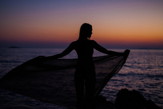 Shadow of a fit girl in the sunset holding a pareo