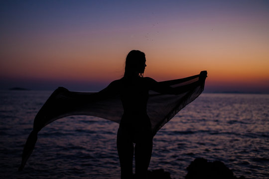 Shadow of a fit girl in the sunset holding a pareo