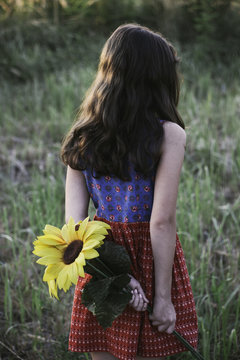 Portrait of a young girl with sunflower from back