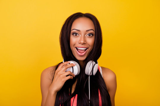Very cheerful emotional dreamy stylish afro lady with bronze skin, long dark hairstyle, so hot, enjoying to the stereo sound in big modern ear phones on her neck, singing, yelling, shouting, pop eyed