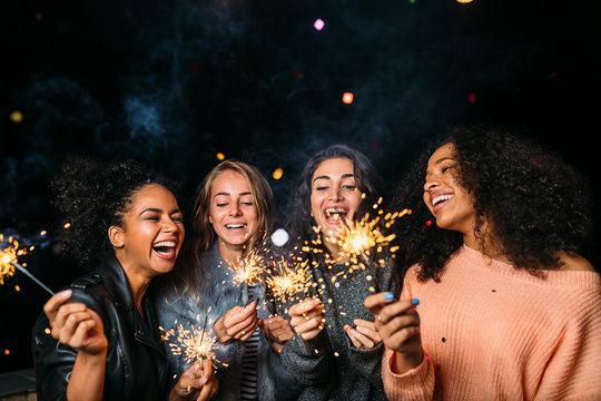 Outdoor shot of laughing friends with sparklers, standing together at night