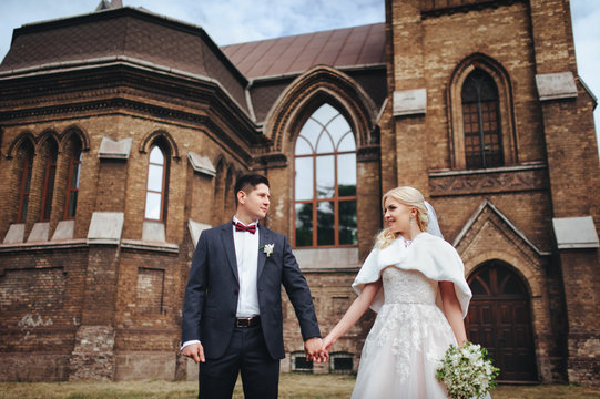 The newlyweds are standing hold hahds on the background of the catalytic church. Catholic temple. Wedding autumn concept.