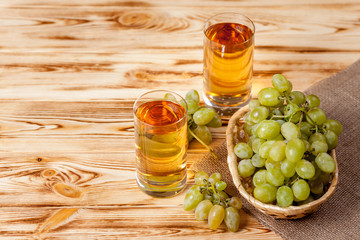 Bunches of fresh ripe green grapes in wicker basket on piece of sackcloth and two glasses with grape juice on a wooden textured backdrop.