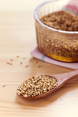 sesame seeds on glass brown bowl and on wood spoon decorated with pink napkin on wood table