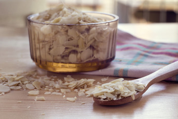 sliced almond on glass brown bowl and on wood spoon decorated with pink napkin on wood table