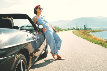 Young woman solo traveler stay near cabriolet car on picturesque mountain road