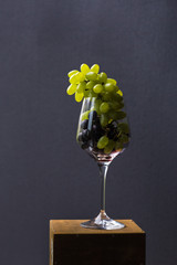 A food photo combines incompatible images. Brushes of red and green grapes in a wine glass look aristocratic and provocative. A top view of a gastronomic ecstasy
