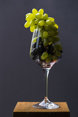 A food photo combines incompatible images. Brushes of red and green grapes in a wine glass look aristocratic and provocative. A top view of a gastronomic ecstasy