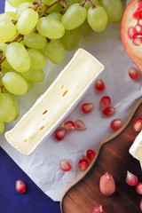 Camembert cheese, orange hard cheese, green grapes, peanuts, walnut and pomegranate seeds on a wooden board on a dark blue background in retro style