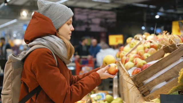 Beautiful Sporty Girl is Choosing Apples on a Stand with Fruits in big Supermarket in Fall