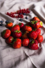 A large guest of juicy red strawberries lies on draped fabric. blueberries, red currants in the background.