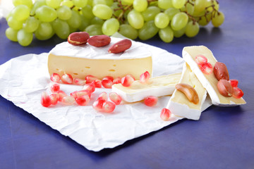 Camembert cheese, sliced cheese, soft cheese with mold, green grapes, peanuts and pomegranate seeds on a dark blue background for labels