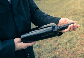 Bottle of red wine in the hands of a man in a black cloak.
