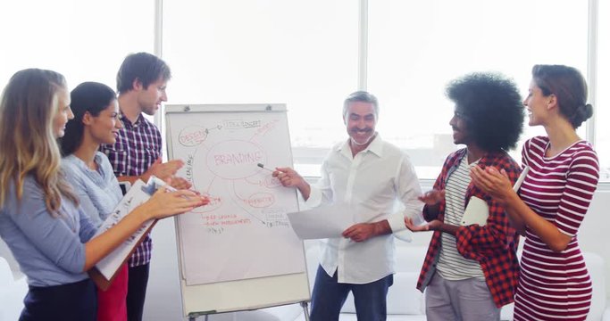 Executives applauding their colleague while giving presentation on flipchart 