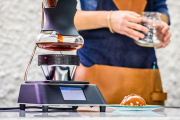 Barista is brewing siphon drip coffee on counter in coffee shop. Alternative methods of coffee brewing.