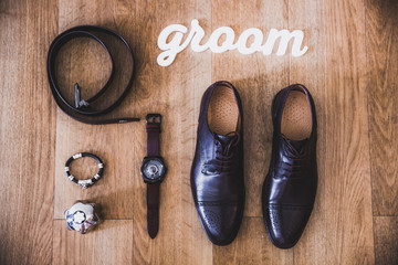 beautiful black leather shoes and other accessories of the groom on the wooden background