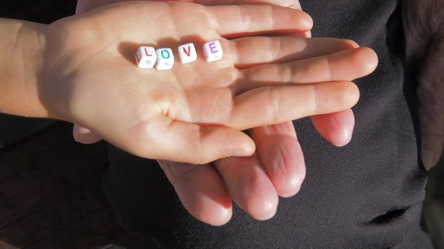 The child's hands hold the word love. The hands of an elderly woman hold the child's hands.