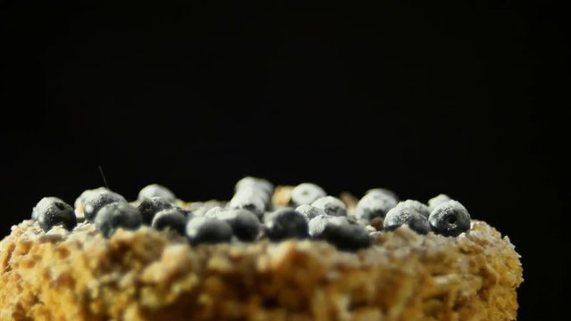 A confectioner, dusting with a powder of sugar glaze over a delicious decadent puff dessert, topped with blueberries at a slowed pace