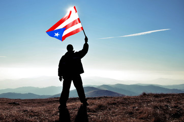 Successful silhouette man winner waving Puerto Rico flag on top of the mountain peak