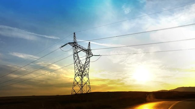 Drive under power line pylon silhouette against sunset