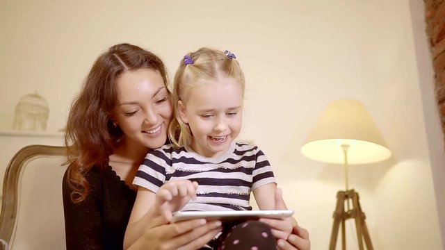 cheerful caucasian mother with her little daughter are watching photos on a tablet