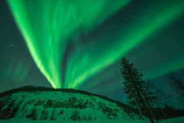 Green aurora fanning across sky over snow-covered hillBo