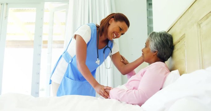 Female doctor comforting senior woman on bed 
