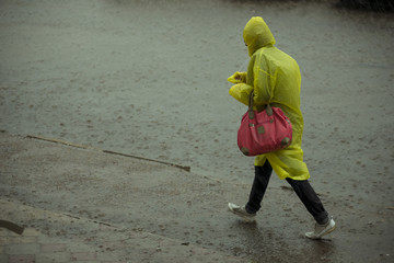 one person in a rain coat of yellow bright color walks along the street wet. very heavy rain and bad weather.