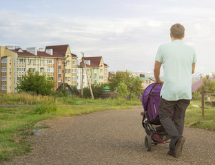 Happy young father walking with a stroller against the background of the city and the beautiful sky.