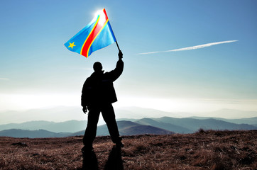 Successful silhouette man winner waving Democratic Republic of Congo flag on top of the mountain...