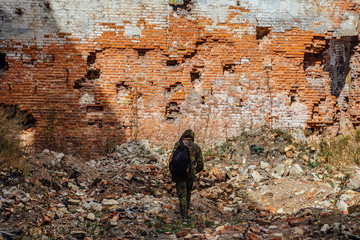 Man in camouflage with a backpack is walking along ruins of city. Post apocalyptic concept 