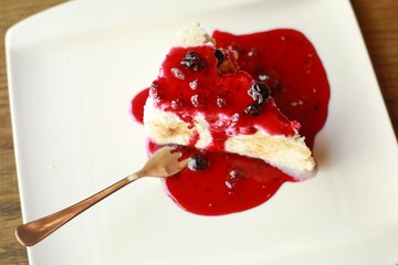 Slice of coconut cheesecake with red fruity topping on white plate with a fork