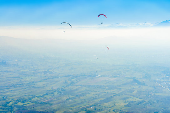 Aerial Pilot pov of three paragliders flying over the mountain foggy valley