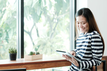 Young asian woman using tablet while sitting by window cafe background, People technology and lifestyle