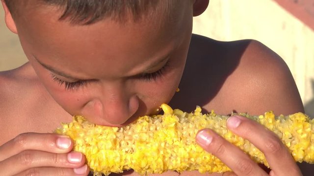 Little hungry refugee boy eating corn on the cob. Focus 