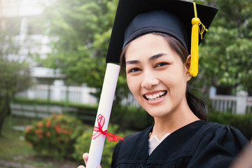 Portrait of young asian woman taking her own photo (selfie) by mobile phone on her graduated day