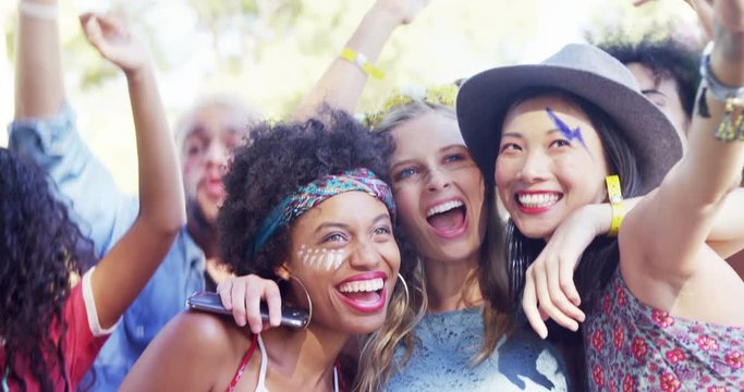 Mixed-race woman friends taking selfie with mobile phone at music festival 