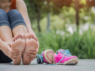 Closeup woman massaging her painful foot while exercising.   Running sport injury concept.