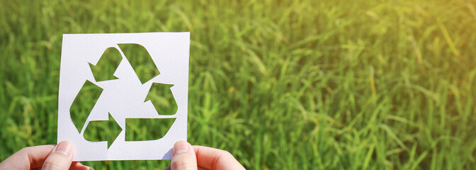 Cut paper with the logo of recycling over green grass. Recycling sign and symbol background banner concept