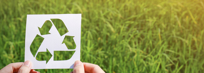 Cut paper with the logo of recycling over green grass. Recycling sign and symbol background banner concept