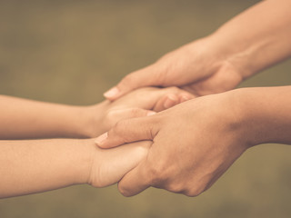 Retro woman  holds the hand of a lovely child. Mother and son holding hands in the background of the green field. People, charity and family concept.