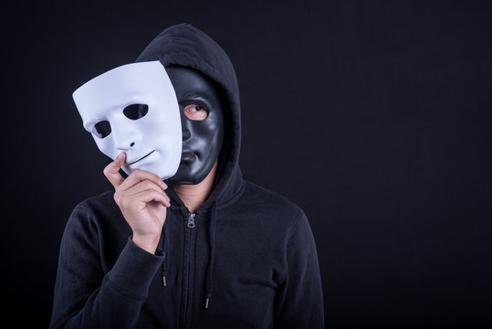 Mystery man wearing black mask holding white mask. Anonymous social masking or halloween concept.