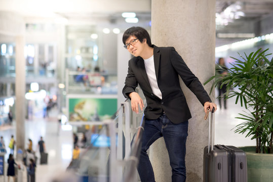 Young asian businessman with his suitcase luggage waiting for airline flight in the international airport terminal, man in business travel concept