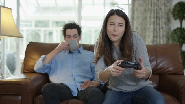  Competitive woman playing video games at home with bored boyfriend beside her
