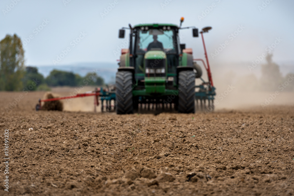 Aufkleber close-up of crop with tractor ploughing field in the background. farmer with tractor seeding.