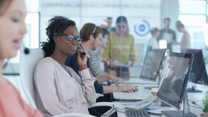  Friendly customer service adviser talking to a customer in busy call center.  - Powered by Adobe
