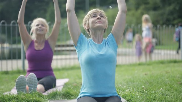  Happy mature female friends doing yoga together in the park