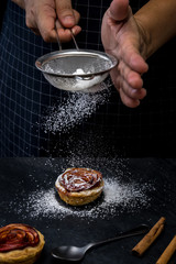action of hand chef sprinkle icing on pie apple rose form. dark food mood tone