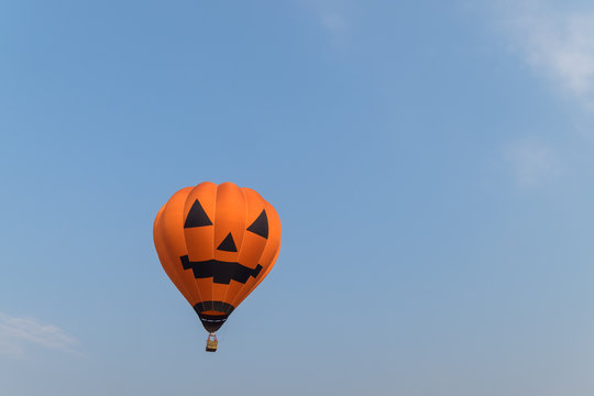 Hot air balloon shaped like a Halloween pumpkin in blue sky background