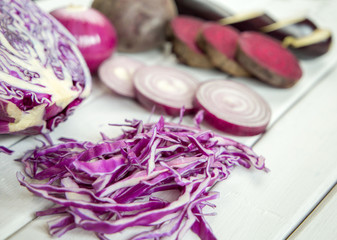 slices of purple vegetables on wooden background - eggplant, beets, basil, onion, cabbage